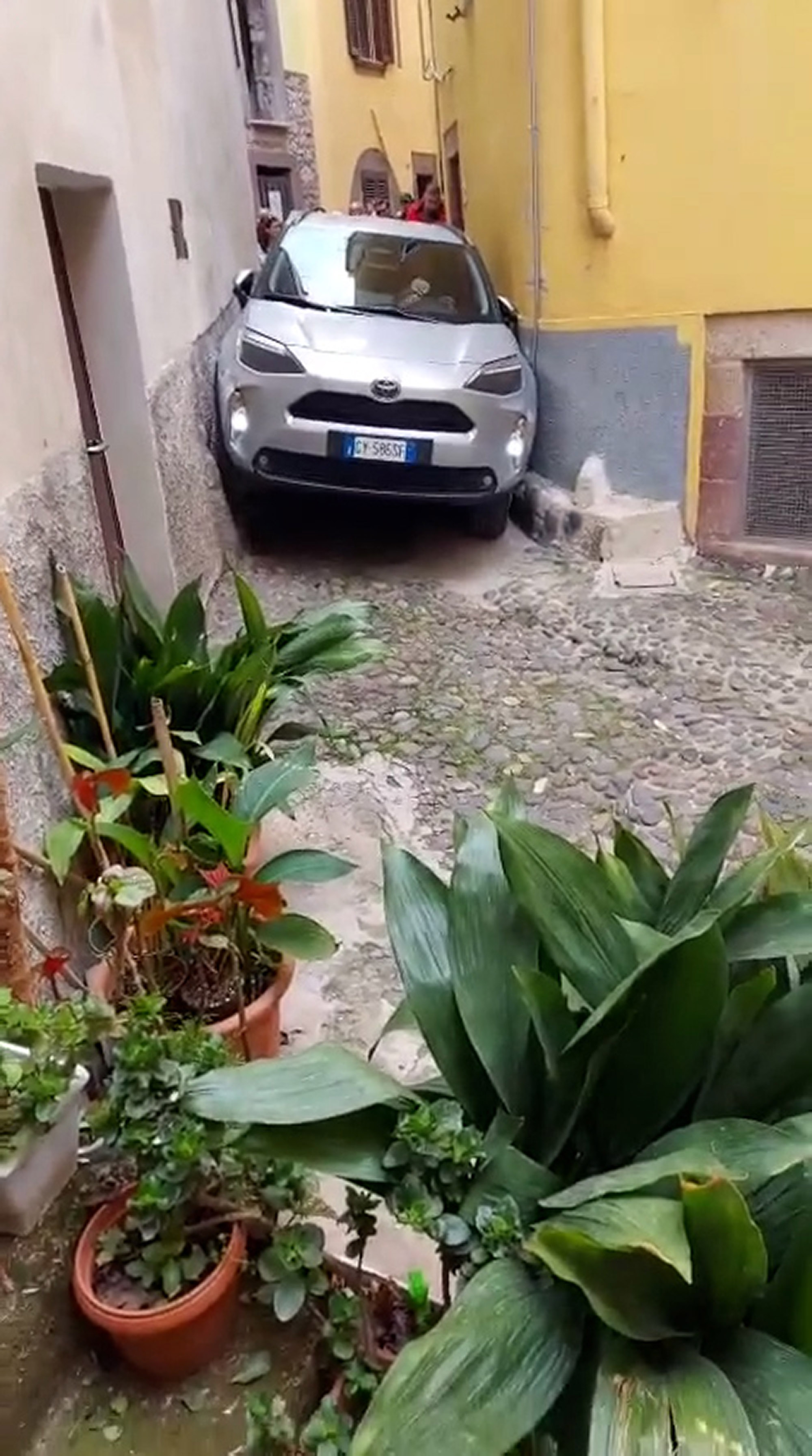 A car gets stuck between two buildings in Bosa, Italy, undated. Passers-by managed to free the car. Note: Photo is a screenshot from a video. A car gets stuck between two buildings