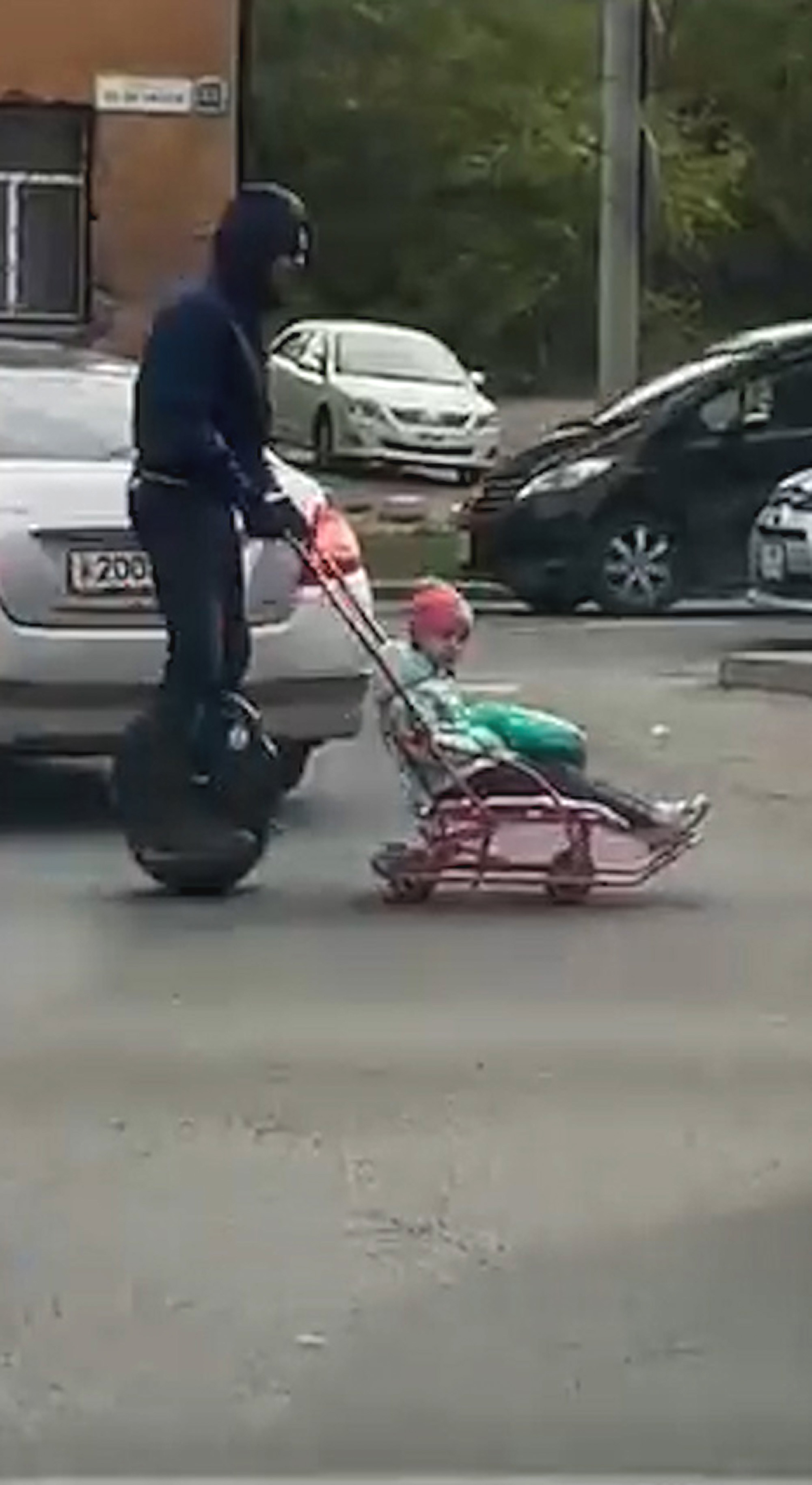 Footage shows a man riding a unicycle and pulling a child on a sled 