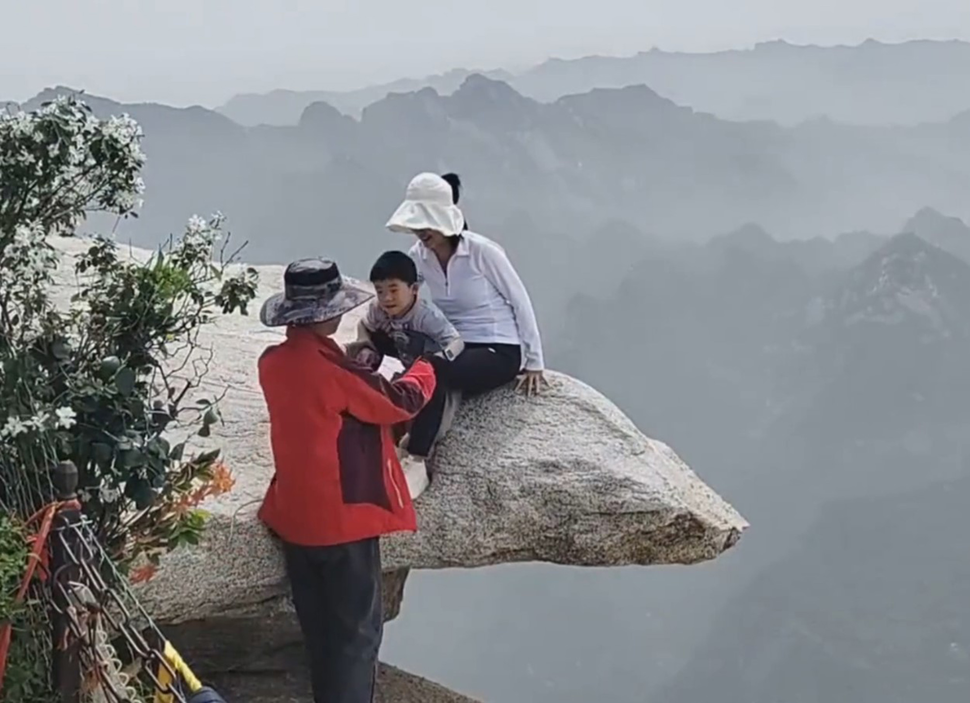 Tourist with child poses for photo on a cliff at the Huashan Scenic Area in Shaanxi Province, China, May 19, 2025. Both were without safety rope. Note: Photo is a screenshot from a video. Tourist with child poses for photo on a cliff
